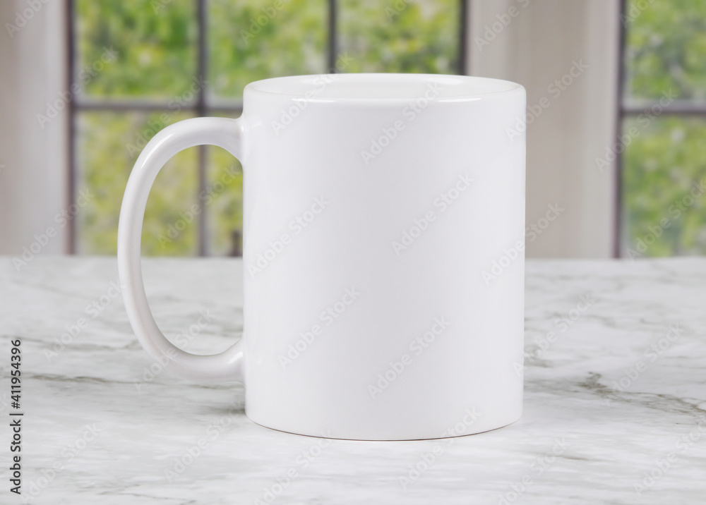 Fototapeta premium White coffee mug with copy space on marble kitchen surface with windows in background