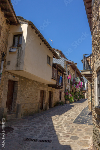 Fototapeta Naklejka Na Ścianę i Meble -  Puebla de Sanabria, Spain - September 6, 2020: Cobblestone street with picturesque stone residential buildings and flowered balconies in Puebla de Sanabría, Zamora province, Castilla y León.