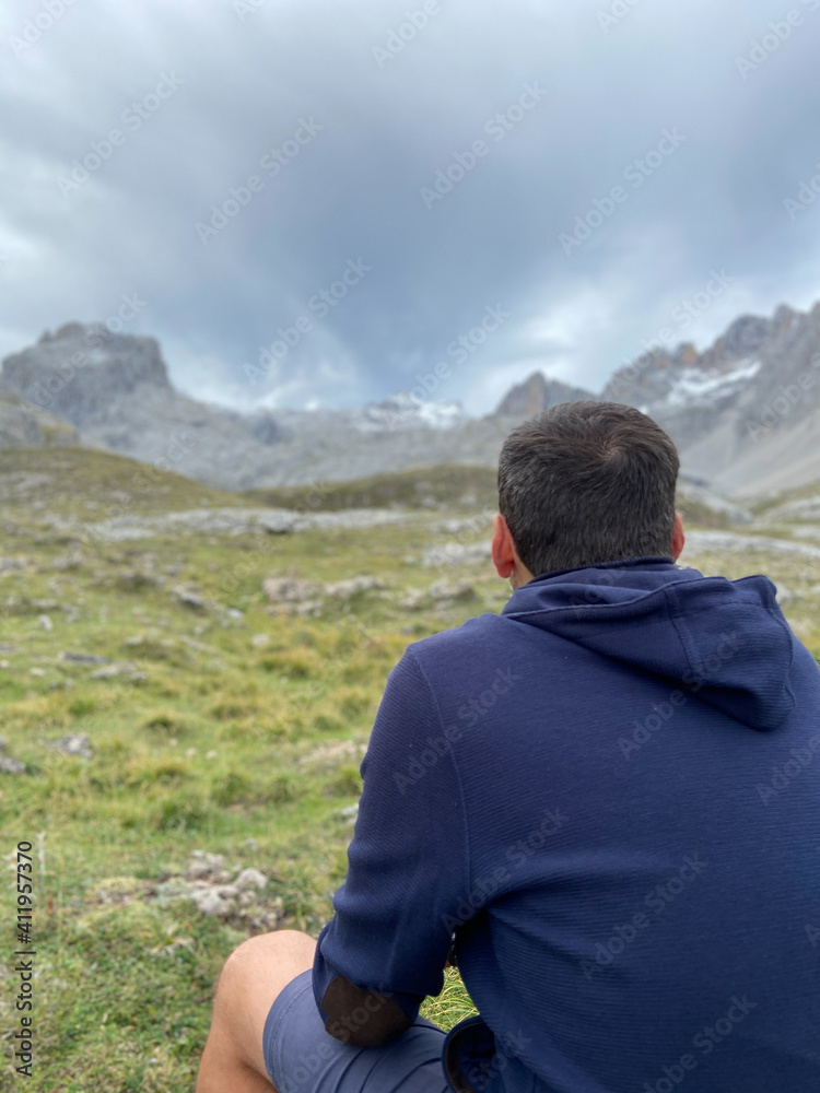Man sitting next to stunning summits of Mounts Pena Remona, Torre de Salinas, La Padierna and Pico de San Carlos at Picos de Europa National Park, Spain.