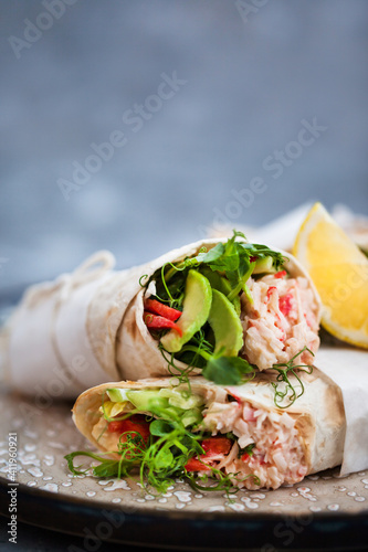 Fresh and healthy wrapped tortilla with crab salad, cucumber, avocado, pepper and green herbs