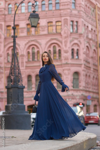 Elegant caucasian woman with long straight brunette hair in blue and white stylish colorful dress walking city street on a bright day