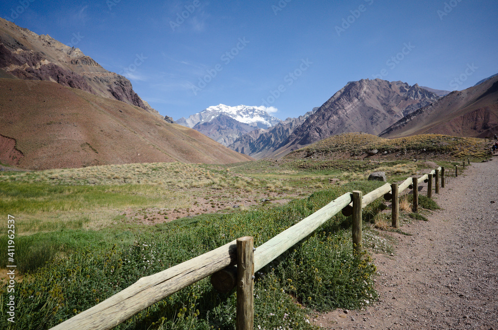 Wooden fence along hiking trail in Aconcagua National Park with view to snow caped highest mountain Andes - Aconcagua peak. Andes Mountains, Mendoza province, Argentina