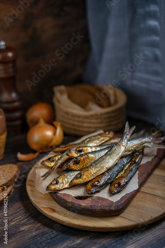 Cold smoked salaka with bread, onion ready to eat. Little golden fish close-up on dark wooden table, healthy natural sea food product, rich of essential Omega-6 fatty acids. Country fisherman style.