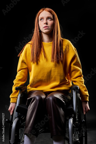 disabled handicapped redhead woman sits looking up, dreaming, having thoughts. isolated black background