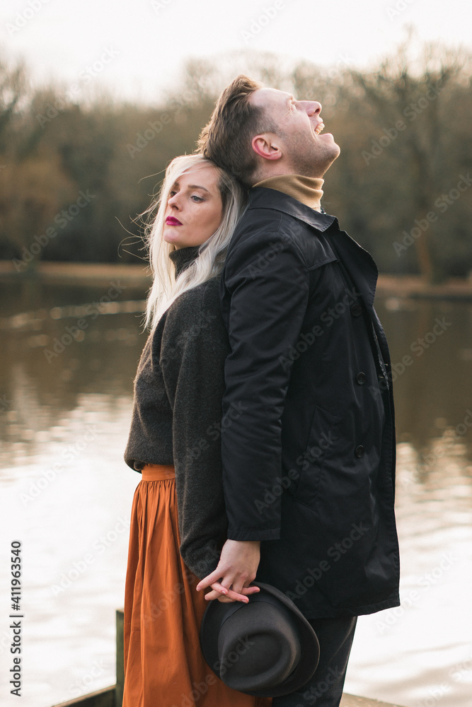 man and woman standing back each other, background lake