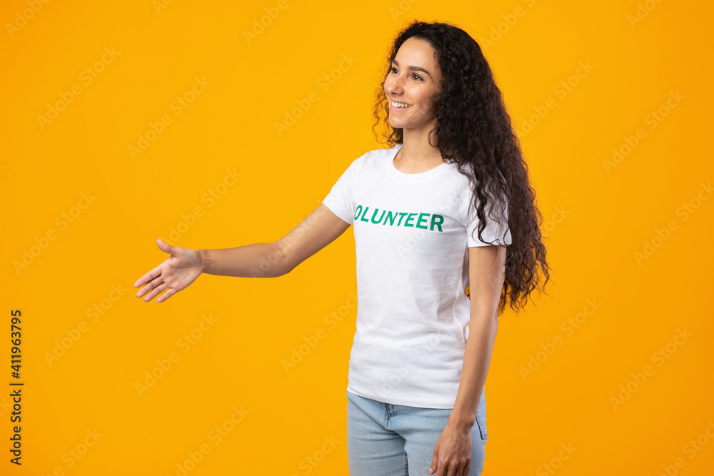 Side-View Of Volunteer Lady Stretching Hand For Handshake, Yellow Background Side-View Of Volunteer Lady Stretching Hand For Handshake, Yellow Background