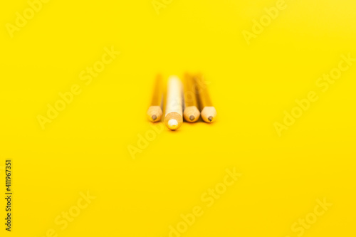 A white pencil that stands out from the crowd of many identical black counterparts on a yellow background. Leadership, uniqueness, independence, initiative, strategy, business success concept