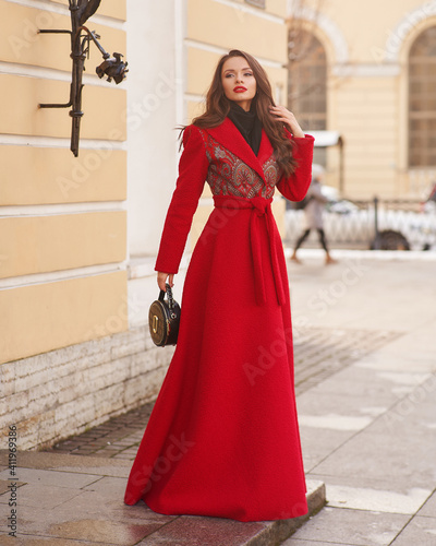 Long-haired woman in red maxi coat and stands near exquisite building © Dmitry Tsvetkov