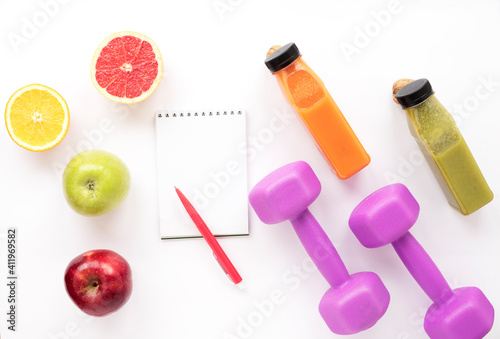 Notepad, dumbbells, fruits, smoothies on a white isolated background. Healthy lifestyle, diet and athletic performance. Top view, flat lay © Olena Poberezhna
