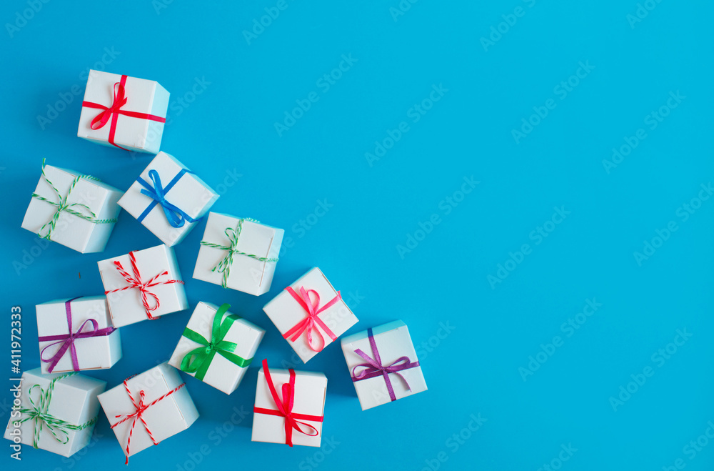 White boxes with colored ribbons lie on a blue background. Top view. Space for the text. White boxes with colored ribbons lie on a blue background. Top view. Space for the text.
