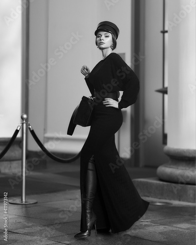 Elegant woman in stylish black maxi dress and cap posing outside exquisite building