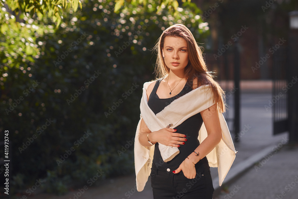 Young woman in black shirt, jeans and white blazer walking and posing outdoors on a summer day. Sun backlight. Outdoor portrait Young woman in black shirt, jeans and white blazer walking and posing outdoors on a summer day. Sun backlight. Outdoor portrait
