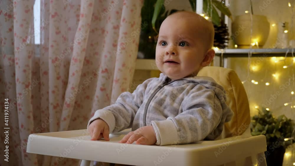 Happy toddler enjoys soap bubbles sitting in a baby's high chair at home. Baby's emotions, home entertainment concept. Happy toddler enjoys soap bubbles sitting in a baby's high chair at home. Baby's emotions, home entertainment concept.