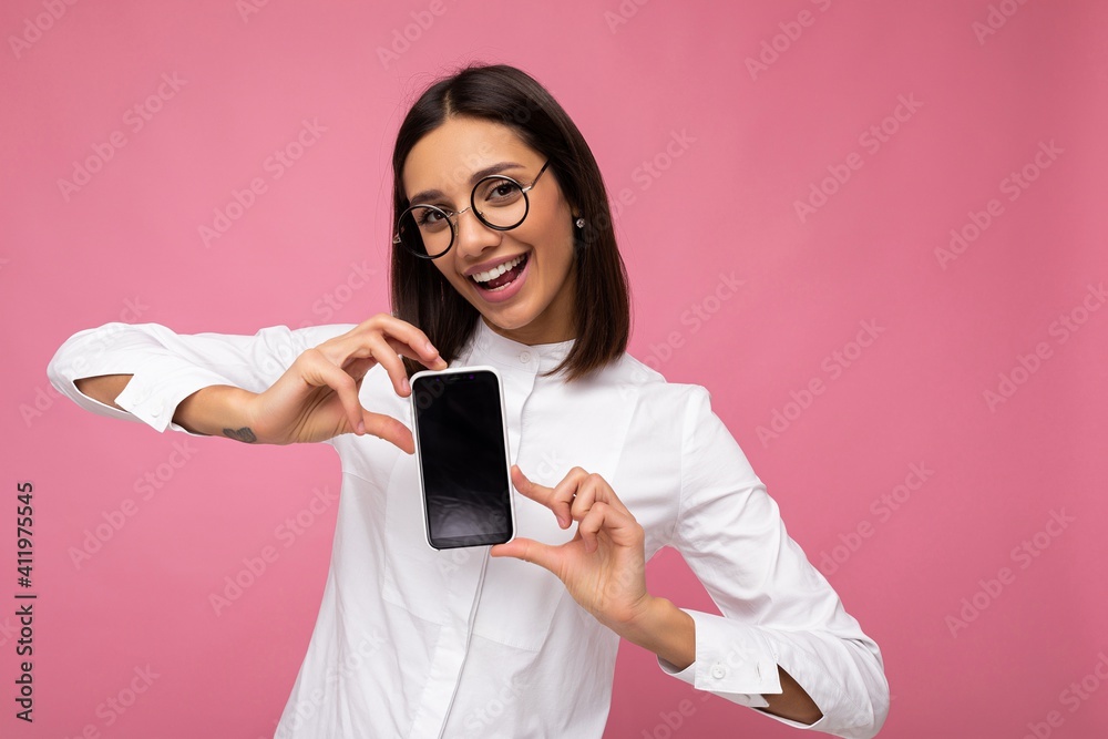 Photo of beautiful smiling young woman good looking wearing casual stylish outfit standing isolated on background with copy space holding smartphone showing phone in hand with empty screen display for Photo of beautiful smiling young woman good looking wearing casual stylish outfit standing isolated on background with copy space holding smartphone showing phone in hand with empty screen display for