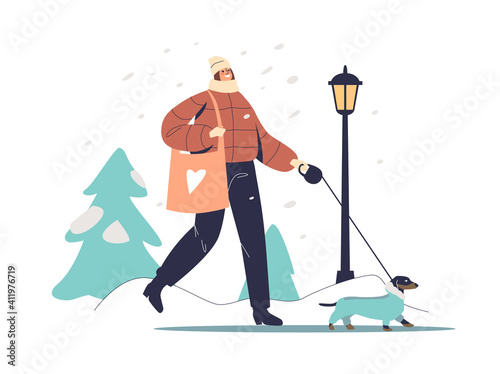 Woman walking with dog in warm coat in winter park over trees in snow