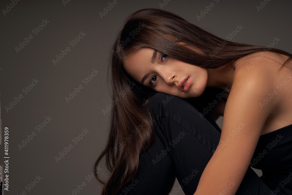 Close-up breast-up portrait of young beautiful brunette teenager girl with long straight hair and perfect natural make-up posing against grey background Close-up breast-up portrait of young beautiful brunette teenager girl with long straight hair and perfect natural make-up posing against grey background