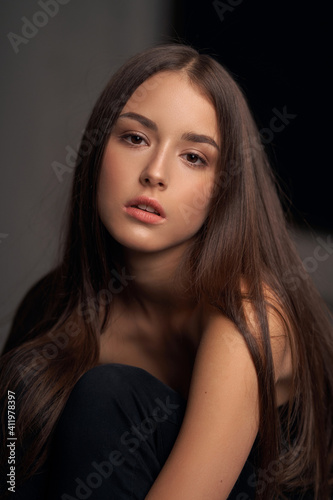 Close-up breast-up portrait of young beautiful brunette teenager girl with long straight hair and perfect natural make-up posing against grey background © Dmitry Tsvetkov