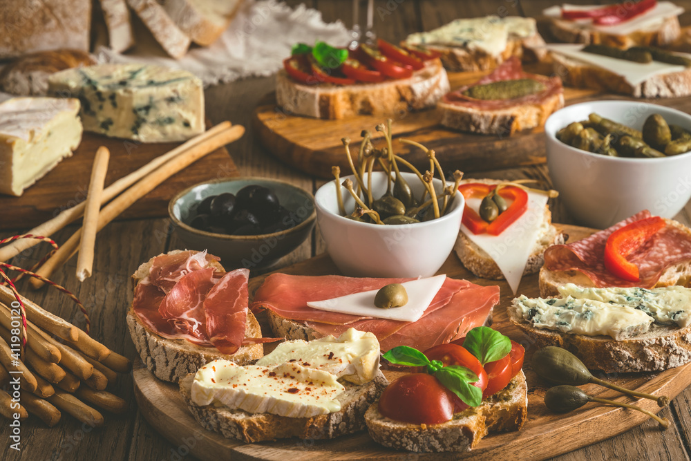 Baguette bread slices with cheese, bacon, salami, olives and capers as a starter, tapas, antipasti, mediterranean style on a rustic wooden table