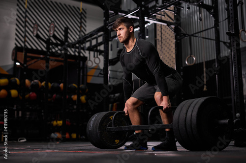 Fotografie strong fit man training with heavy weights at gym, young caucasian guy in black sportswear do workout exercises alone