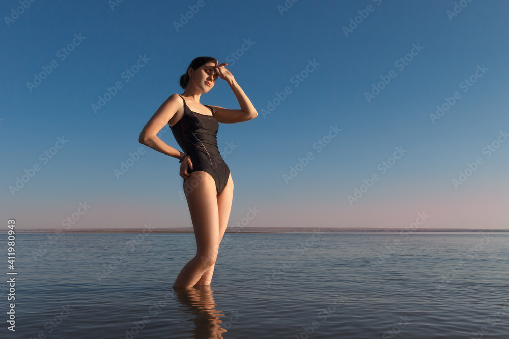 Summer vacation concept. Young beautiful slim woman wearing a black swimsuit stands in the sea and watching sunset. Copy space Summer vacation concept. Young beautiful slim woman wearing a black swimsuit stands in the sea and watching sunset. Copy space