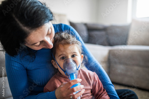 Mother helps her little girl to makes inhalation at home.During coronavirus COVID-19 photo