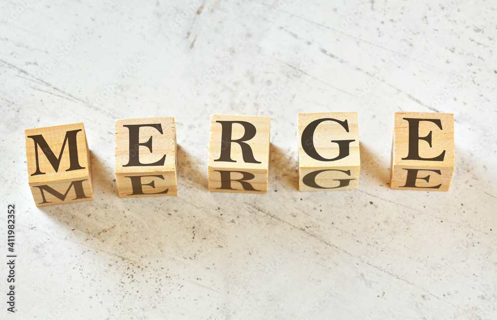 Five wooden cubes with word MERGE on white stone like board, view from above Five wooden cubes with word MERGE on white stone like board, view from above