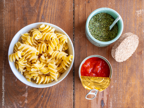 Top view of ingredients for pasta recipe. Fusilli giganti in a bowl with fried tomato in a can and oregano in a jar. High resolution