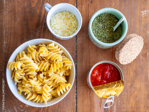 Top view of ingredients for pasta recipe. Fusilli giganti in a bowl with fried tomato in a can with oregano in a jar with cheese in a pot. High resolution