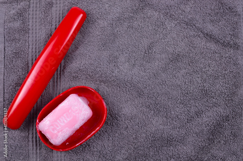 a toothbrush case and an open red soap dish with pink soap are on a gray towel