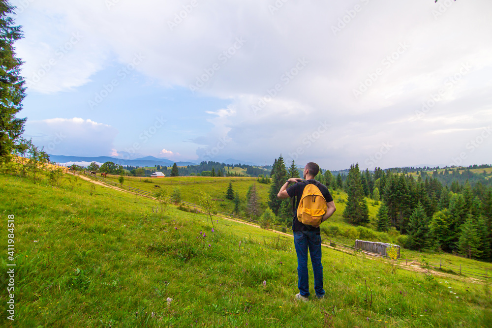 A guy travels with a yellow backpack through picturesque places with beautiful mountain landscapes