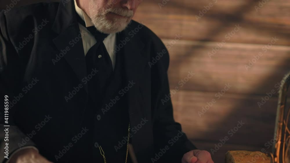 Overhead window light illuminates this 19th century scene that moves down from  a pensive gentleman checking the time on his pocket watch to other items on a rustic table he is standing next to.