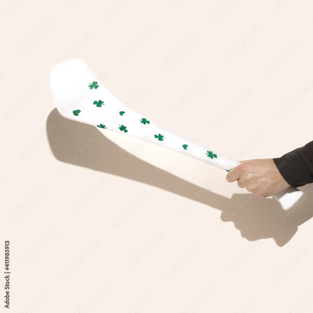 A male hand holding white hurling stick, hurley with  with shamrock decoration. Beige background.