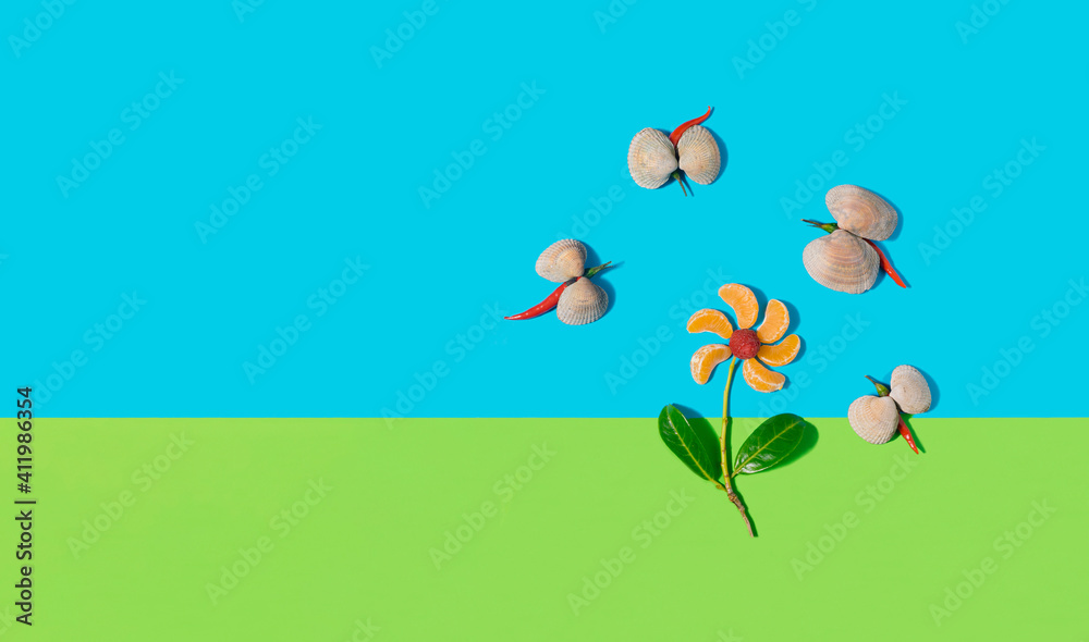 Fototapeta premium Arrangement created from tangerine slices with raspberry in the middle. Sea shells and chilli peppers peppers assembled together. From above on green and blue background. Copy space for text.