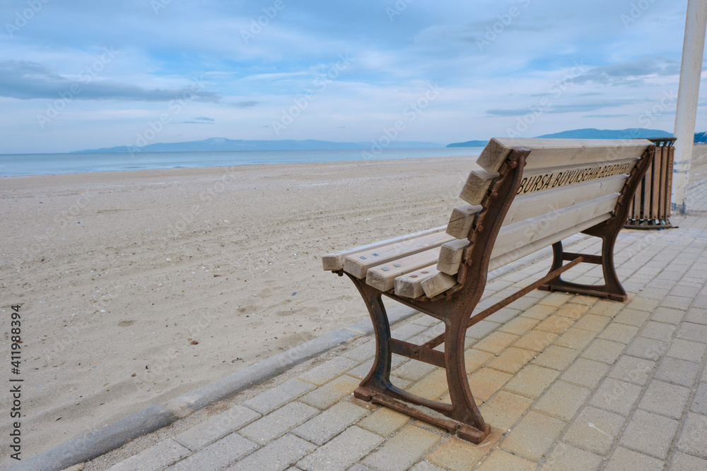 Great sea view, and beach together with wooden bench and its metal side exposed to corrosion and remainings of corrosion. Magnificent sky background. Street bench standing on cobblestone pathway. Great sea view, and beach together with wooden bench and its metal side exposed to corrosion and remainings of corrosion. Magnificent sky background. Street bench standing on cobblestone pathway.