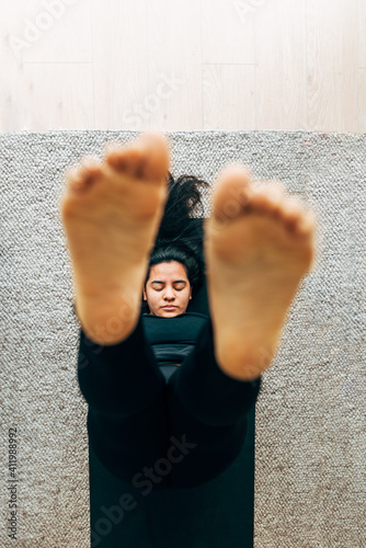 Latin woman lying on the floor while stretching her feet practicing yoga