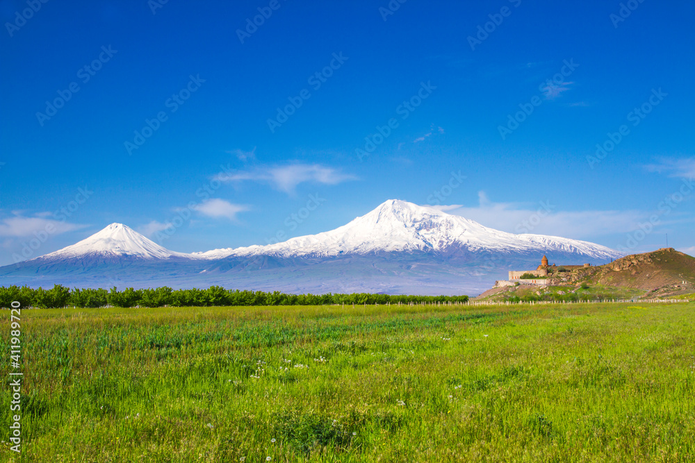 Fototapeta premium Awe-Inspiring medieval Khor Virap monastery in front of Mount Ararat viewed from Yerevan, Armenia. This snow-capped dormant compound volcano described in the Bible as the resting place of Noah's Ark.