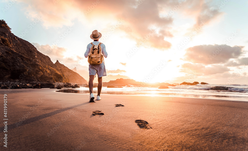 Plakat Man with backpack walking on the beach at sunset - Travel lifestyle concept - Golden filter