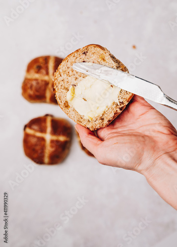 Woman hand holding traditional Easter hot cross bun with butter and knife