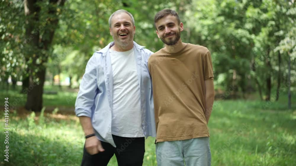 Portrait of joyful Caucasian men having fun talking and laughing in sunny summer park. Cheerful young son and middle aged father resting outdoors on weekend, Family unity concept. Portrait of joyful Caucasian men having fun talking and laughing in sunny summer park. Cheerful young son and middle aged father resting outdoors on weekend, Family unity concept.