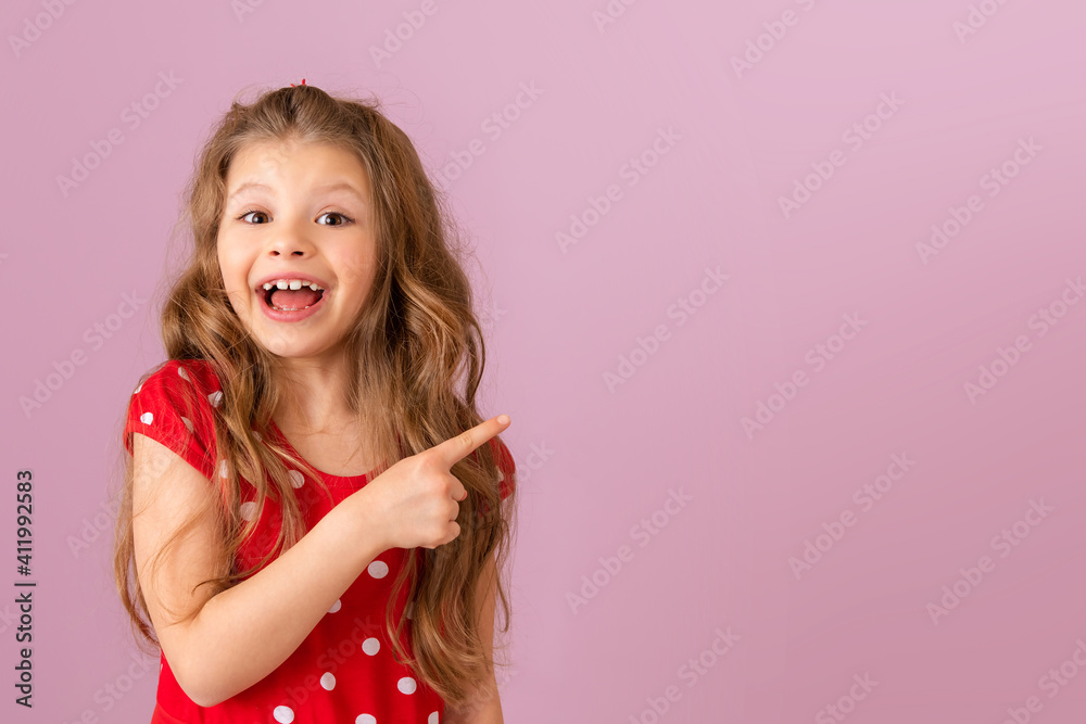 A little girl with curly hair points her finger to the side. Copy space. A little girl with curly hair points her finger to the side. Copy space.