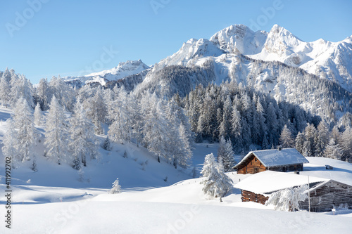 Beautiful winter mountain landscape with snowy forest and traditional alpine chalet. Sunny frosty weather with clear blue sky 