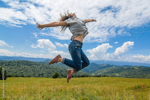 Happy gorgeous girl enjoy mountain view jumping on the hill with breathtaking mountain landscape