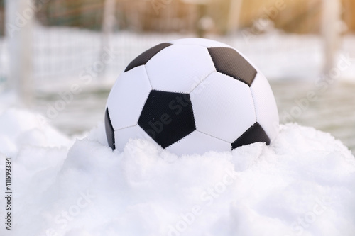 Soccer ball placed on snowdrift near goal in winter on synthetic sports ground at sunny day © Serhii