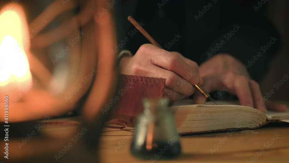 Nineteenth century type scene lit by the light from an oil lamp of a man writing in a journal using a dip pen.