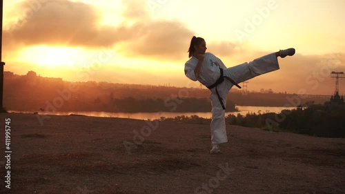 Translation: Kyokushinkai. girl warms up, trains stretching, kick in karate. Harmony with nature. Autumn at sunset. In the background, the golden river, the sun forest, the bridge, the city, the photo