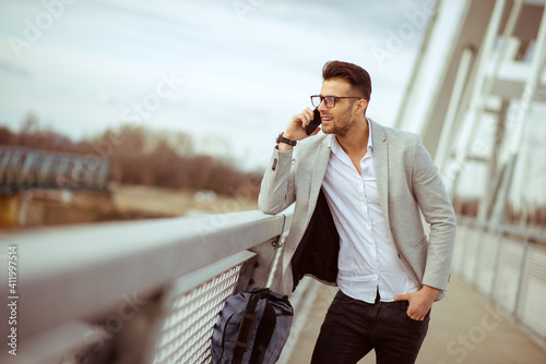 Young businessman talking on cell phone on the bridge. Satisfied yuppie smiling and enjoying outdoors photo