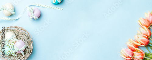Photography Golden easter colour eggs in basket with spring tulips, white feathers on pastel blue background in Happy Easter decoration