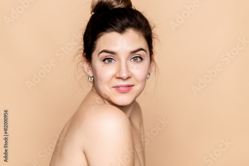 Beauty feminine portrait of female face with healthy natural skin. Beautiful tanned girl with brown hair looking at camera. Pretty attractive young woman posing at studio on beige studio background