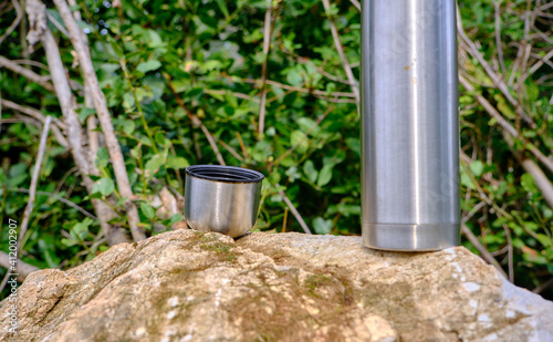 Caffe mug and heat sealing thermos cover made of stainless steel on thee rock by taking photo during trekking in wild nature in forest