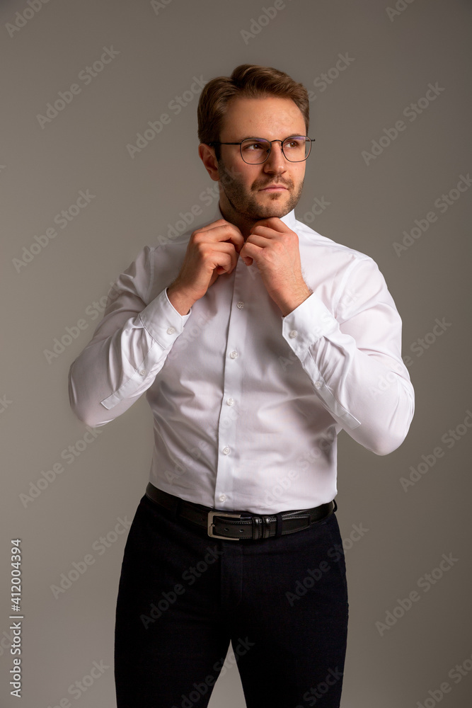 Fototapeta premium A man in a white shirt, dark trousers, black boots and glasses stands against a plain background, looking away. Business clothes. Confident look. Success